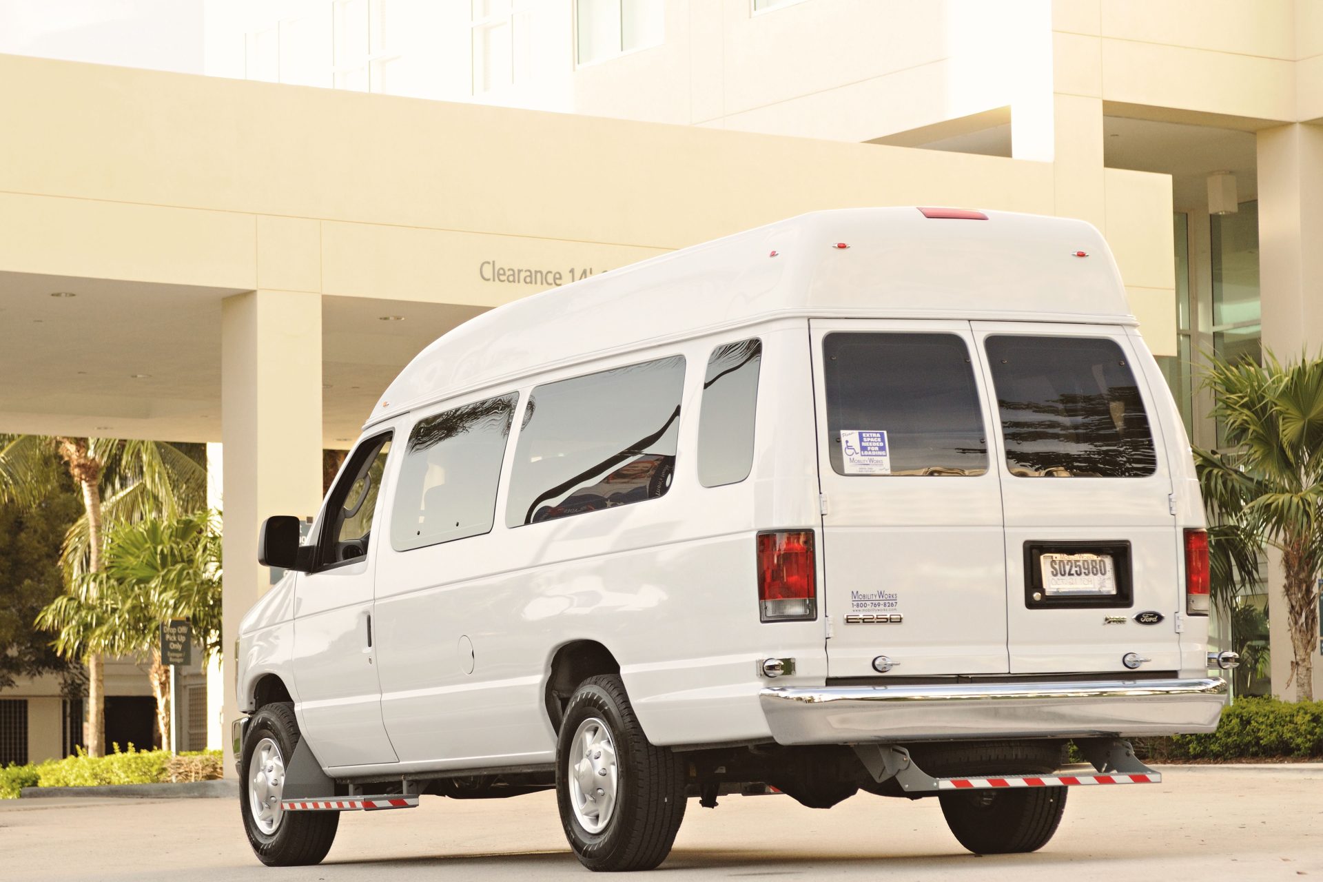A white passenger van parked outside a modern building with palm trees in the background.
